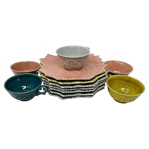 May include: A collection of vintage ceramic dishware in various colors. The set includes leaf-shaped plates, teacups, and bowls in shades of pink, green, teal, and yellow. The teacups and bowls have a textured, embossed design.