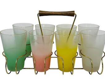 May include: A vintage set of six frosted glass tumblers in a gold-toned metal carrier with a wooden handle. The glasses are in shades of green, pink, yellow, and white. A stylish addition to any home bar.