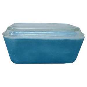 May include: A rectangular, teal-colored casserole dish with a clear glass lid. The dish has a slightly tapered shape and a smooth, glossy finish. The lid fits snugly on top, creating a complete seal. This vintage kitchenware is perfect for baking and serving.