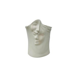 May include: A matte white ceramic vase featuring a sculptural design with two overlapping human faces embossed on the front surface. The vessel has a smooth, curved silhouette with an asymmetrical top edge and a solid, opaque finish throughout.