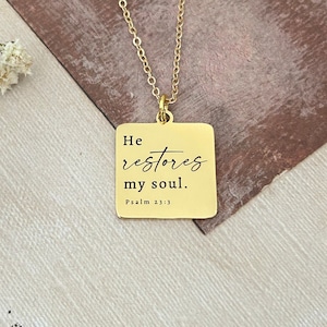 Op de afbeelding: Gouden ketting met een vierkante hanger met de tekst "Hij herstelt mijn ziel. Psalm 23:3"