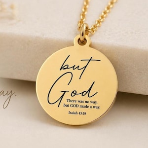 Op de afbeelding: Een goudkleurige ronde hanger aan een ketting met de gegraveerde zwarte tekst "but God" in een cursief lettertype, gevolgd door de kleinere tekst "There was no way, but GOD made a way. Isaiah 43:19" in een strak schreefloos lettertype.