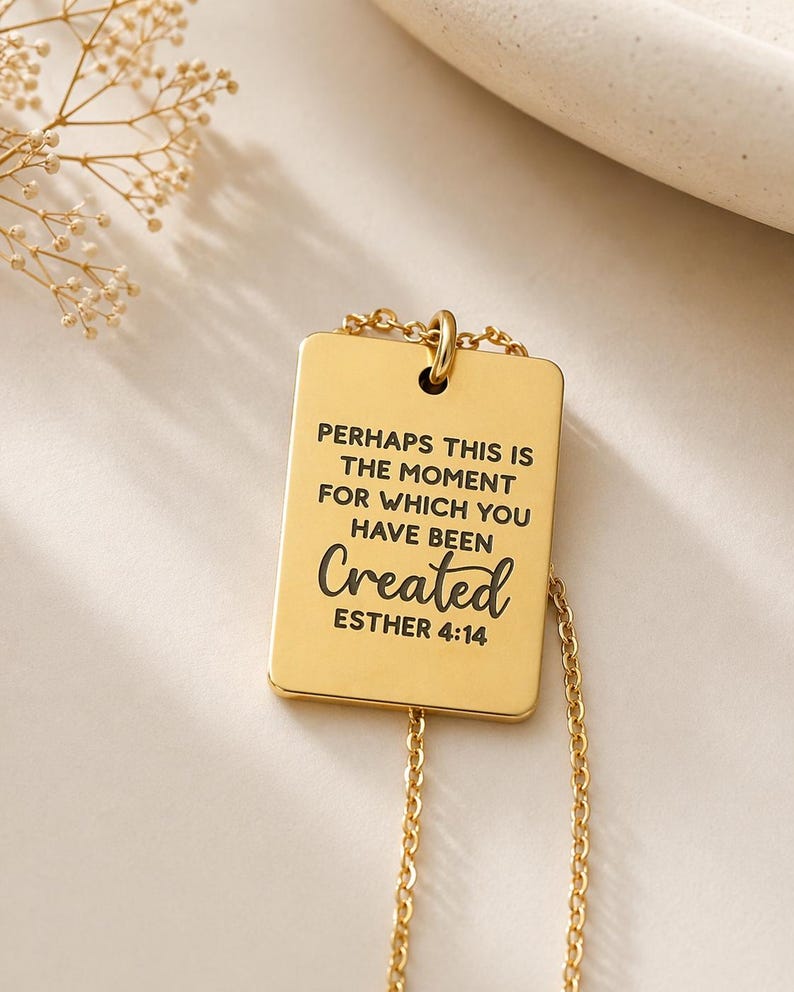 Op de afbeelding: Een goudkleurige rechthoekige hanger aan een ketting met de gegraveerde zwarte tekst: PERHAPS THIS IS THE MOMENT FOR WHICH YOU HAVE BEEN Created ESTHER 4:14. De hanger hangt aan een fijne goudkleurige ketting en heeft een gladde afwerking.