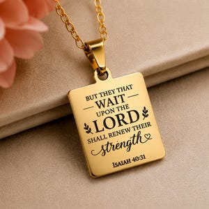 Op de afbeelding: Een goudkleurige rechthoekige hanger aan een bijpassende ketting met de gegraveerde zwarte tekst: BUT THEY THAT WAIT UPON THE LORD SHALL RENEW THEIR STRENGTH ISAIAH 40:31, versierd met kleine bladmotieven en een hartsymbool.