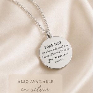 May include: A silver-toned circular pendant necklace featuring the engraved text FEAR NOT for I have redeemed you I have called you by name you are mine Isaiah 43:1. The pendant hangs from a delicate silver-toned chain link necklace.