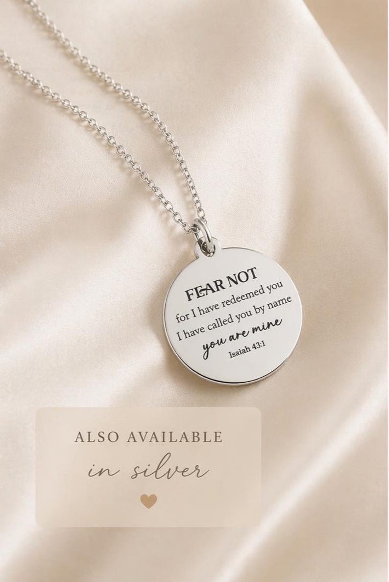 May include: A silver-toned circular pendant necklace featuring the engraved text FEAR NOT for I have redeemed you I have called you by name you are mine Isaiah 43:1. The pendant hangs from a delicate silver-toned chain link necklace.