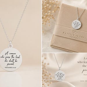 Op de afbeelding: Een zilverkleurige ketting met een ronde hanger waarop de tekst A woman who fears the Lord, she shall be praised, Proverbs 31:30 is gegraveerd. De ketting wordt getoond aan een dunne ketting, vergezeld door een beige geschenkdoos met merknaam.