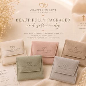 May include: Five small, square, velvet-textured jewelry pouches in cream, dusty pink, sage green, taupe, and light gray. Each pouch features a flap closure with the text Wrapped in Love Charms and a double heart logo printed in a dark color.