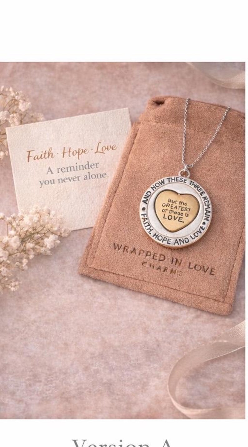 May include: A silver necklace with a heart-shaped pendant, inscribed with "But the GREATEST of these is LOVE." The pendant is on a chain, displayed with a card that reads "Faith Hope Love" and a reminder message. The necklace is in a tan pouch.