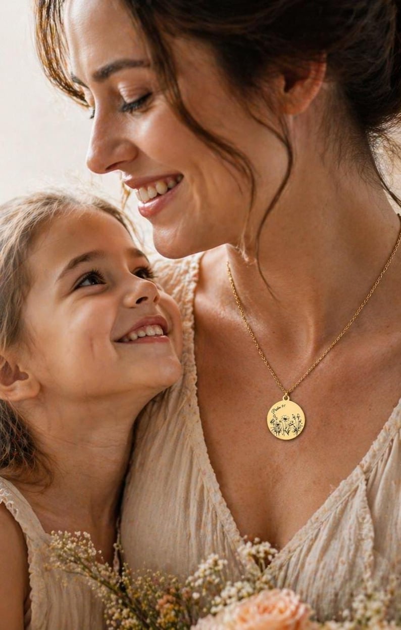 Op de afbeelding: Een goudkleurige ronde hanger aan een ketting met een fijne zwarte lijntekening van wilde bloemen en de tekst Psalm 91 gegraveerd op het oppervlak. De hanger hangt aan een bijpassende goudkleurige ketting tegen een lichtgekleurde stof.