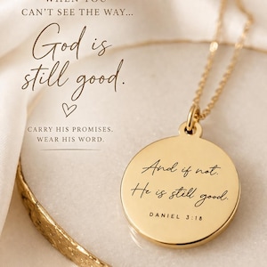 Op de afbeelding: Een goudkleurige ronde hanger aan een ketting met de gravure 'And if not. He is still good. DANIEL 3:18'. De hanger hangt aan een fijne gouden ketting. De tekst 'WHEN YOU CAN'T SEE THE WAY... God is still good. CARRY HIS PROMISES. WEAR HIS WORD.' is zichtbaar.