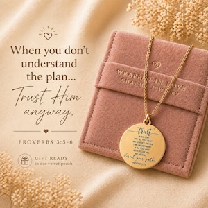 Könnte beinhalten: Eine goldfarbene Halskette mit Anhänger und einem runden Charm, auf dem das Wort "trust" und ein Bibelvers eingraviert sind. Die Halskette liegt auf einem rosa Samtbeutel. Der Text "When you don't understand the plan... Trust Him anyway" ist ebenfalls sichtbar.