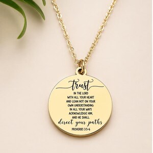 May include: A gold-toned circular pendant necklace featuring the engraved text Trust in the Lord with all your heart and lean not on your own understanding in all your ways acknowledge him, and he shall direct your paths Proverbs 3:5-6.