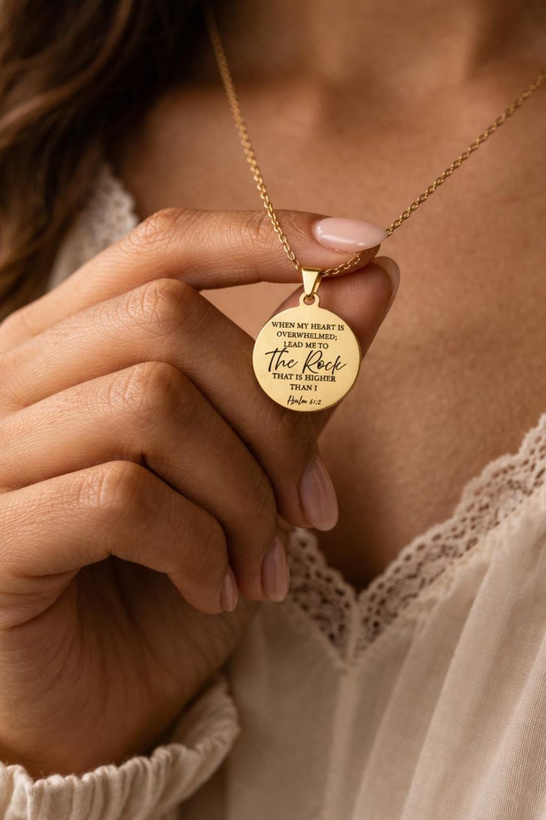 Op de afbeelding: Een goudkleurige ronde hanger aan een ketting met de gegraveerde tekst: WHEN MY HEART IS OVERWHELMED; LEAD ME TO The Rock THAT IS HIGHER THAN I Psalm 61:2. De hanger hangt aan een fijne goudkleurige ketting met een gepolijste metalen afwerking.