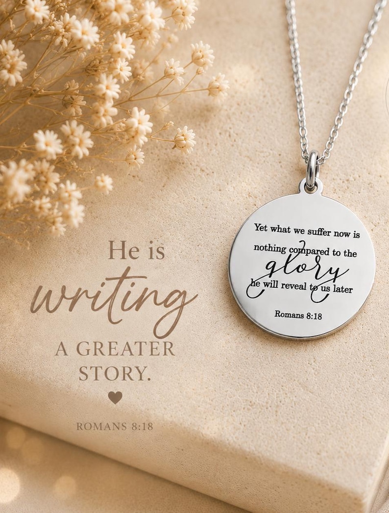 May include: A silver-toned circular pendant necklace featuring the engraved text: Yet what we suffer now is nothing compared to the glory he will reveal to us later Romans 8:18. The pendant hangs from a delicate silver chain against a neutral background.