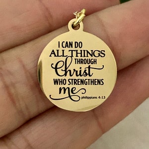 May include: A gold-colored round pendant with the inscription "I CAN DO ALL THINGS THROUGH Christ WHO STRENGTHENS me" and "philippians 4:13" in black lettering. The pendant has a small loop at the top for a chain.
