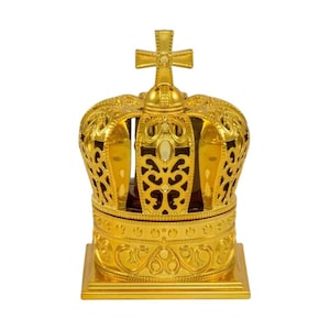 Puede incluir: Una caja decorativa dorada en forma de corona con una cruz en la parte superior. La corona tiene intrincados patrones de filigrana y se asienta sobre una base cuadrada. La caja está hecha de un material metálico brillante.