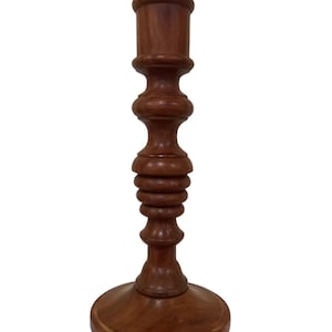 May include: A dark brown wooden candle holder with a simple, elegant design. The holder has a round base and a tall, slender stem with a decorative, fluted section.