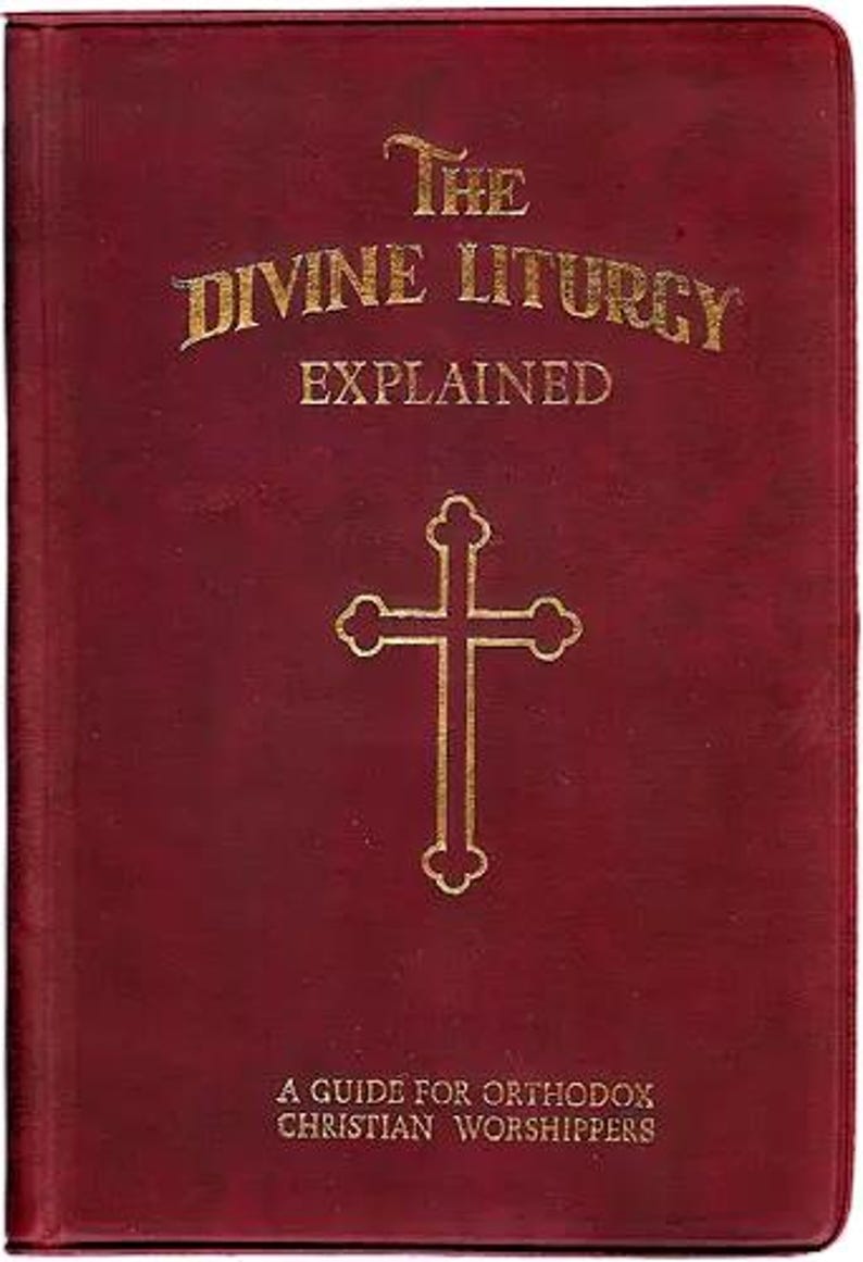 Pu&ograve; includere: Un libro bordeaux intitolato "The Divine Liturgy Explained" con lettere dorate e una croce dorata. &Egrave; una guida per i fedeli cristiani ortodossi. La copertina ha un aspetto strutturato.