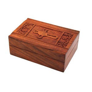 May include: A rectangular wooden box with a hinged lid. The box is a warm brown color and features carved floral designs on the top and sides. A decorative metal clasp is centered on the lid. The box is likely used for storing small items.