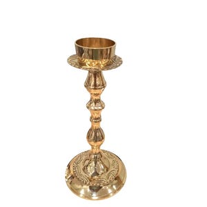 May include: A gold-colored candlestick holder with a round base and a decorative design. The candlestick has a tall, ornate stem and a circular top to hold a candle. The overall design is elegant and classic.