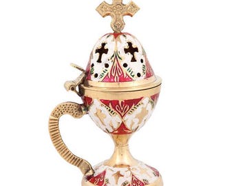 May include: A gold-colored censer with a cross on top, featuring red, white, and gold floral patterns. The censer has a handle and a decorative base, suitable for religious ceremonies.