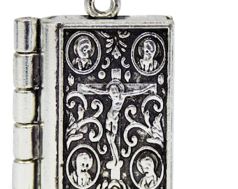 May include: A silver charm in the shape of a closed book with a crucifix and four figures on the front. The book charm has a hinged side and a loop at the top for attaching to a bracelet or necklace.