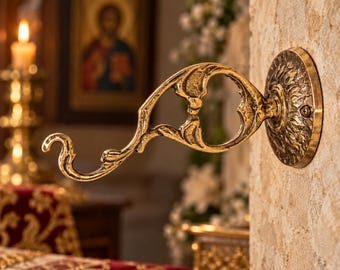 Può includere: Un gancio da parete in ottone caratterizzato da un design curvo e ornato con una piastra di base circolare. Il metallo presenta una finitura lucida e riflettente con dettagli in rilievo lungo il braccio e la piastra di montaggio.
