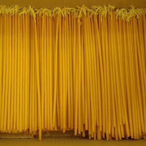 Puede incluir: Primer plano de una caja llena de muchas velas finas de cera de abeja amarilla. Las velas están dispuestas en filas y todas tienen la misma longitud.