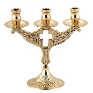 Könnte beinhalten: Ein goldfarbener Kerzenständer für drei Kerzen mit einem kreuzförmigen Ausschnitt in der Mitte. Der Kerzenständer hat ein dekoratives Blumendesign und einen runden Sockel. Jeder Kerzenhalter hat eine kleine, runde Platte.