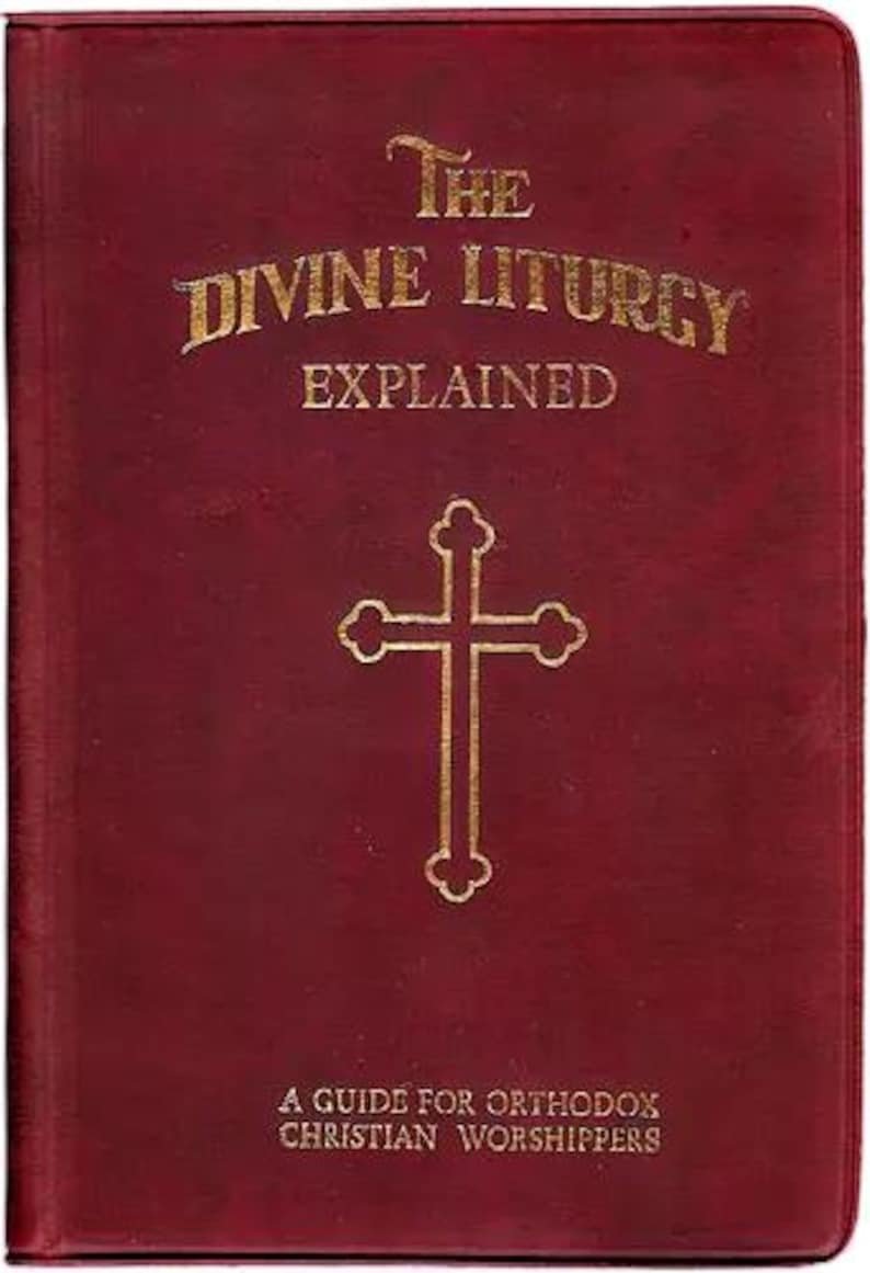 Pu&ograve; includere: Un libro bordeaux intitolato "The Divine Liturgy Explained" con lettere dorate e una croce dorata. &Egrave; una guida per i fedeli cristiani ortodossi. La copertina ha un aspetto strutturato.