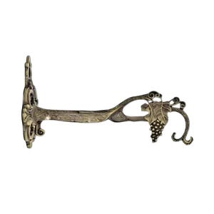 Op de afbeelding: Een bronzen wandbeugel in antieke stijl. Het heeft een decoratief ontwerp met een druiventros en bladmotief. De beugel is ontworpen om een ​​item vast te houden en heeft een sierlijk, opgerold ontwerp.