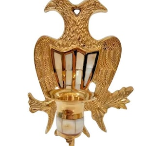 Könnte beinhalten: Goldfarbener Wand-Kerzenhalter mit zwei stilisierten Vögeln, die sich gegenüberstehen. Die Vögel haben ein Perlmutt-Inlay-Design.