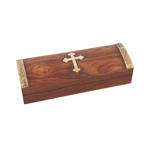Könnte beinhalten: Eine rechteckige Holzkiste mit einem Messingkreuz auf dem Deckel. Die Kiste ist dunkelbraun mit Messingakzenten an den Ecken. Die Kiste wird wahrscheinlich für religiöse Zwecke verwendet.