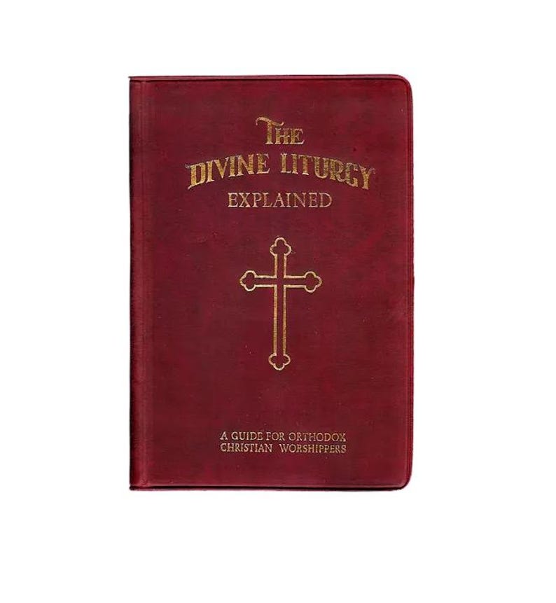 Pu&ograve; includere: Un libro bordeaux intitolato "The Divine Liturgy Explained" con lettere dorate e una croce dorata. La copertina del libro include anche il testo "A Guide for Orthodox Christian Worshippers".