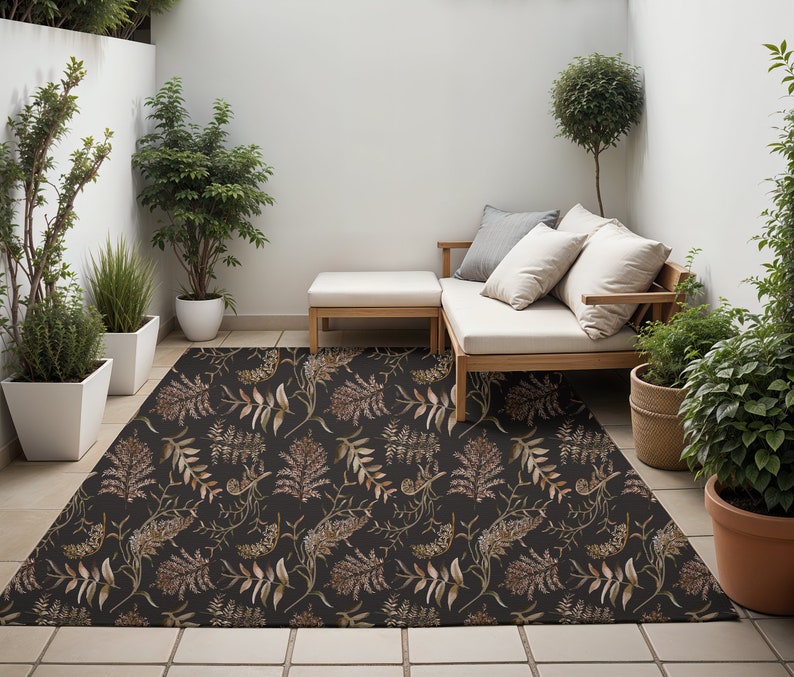 May include: A black and brown floral patterned outdoor rug with a white couch and two pillows, a wooden coffee table, and potted plants in the background.