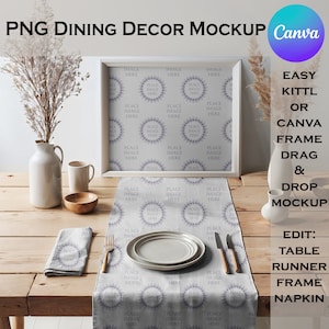 May include: A white framed picture sits on a wooden table with a white table runner with a repeating pattern. A white plate, fork, and knife are on the table runner. A white napkin is folded on the table runner. A white vase with dried flowers and a white mug are on the table.