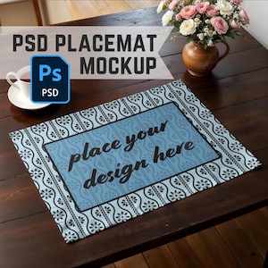 Puede incluir: Una maqueta de mantel individual azul y negro con el texto "place your design here" en un rectángulo blanco. El mantel individual está sobre una mesa de madera con una taza de té y un jarrón de flores.