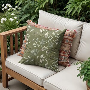 May include: A wooden outdoor sofa with white cushions and three throw pillows. The pillows have a green leafy pattern, a pink and orange floral pattern, and a colourful geometric pattern.