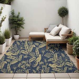 May include: A navy blue outdoor rug with a pattern of gold leaves, birds, and flowers. The rug is placed on a patio with a wooden bench and potted plants.