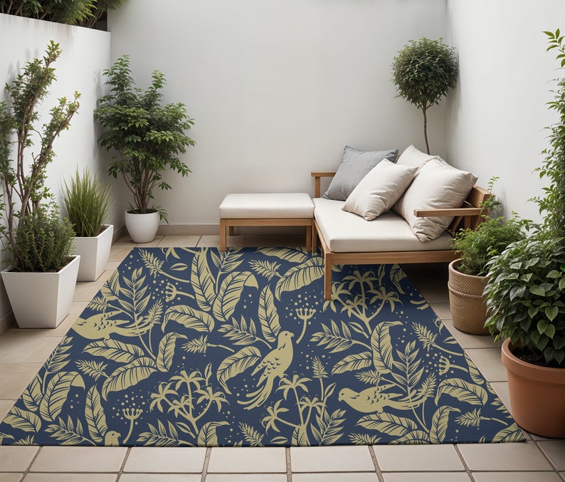 May include: A navy blue outdoor rug with a pattern of gold leaves, birds, and flowers. The rug is placed on a patio with a wooden bench and potted plants.