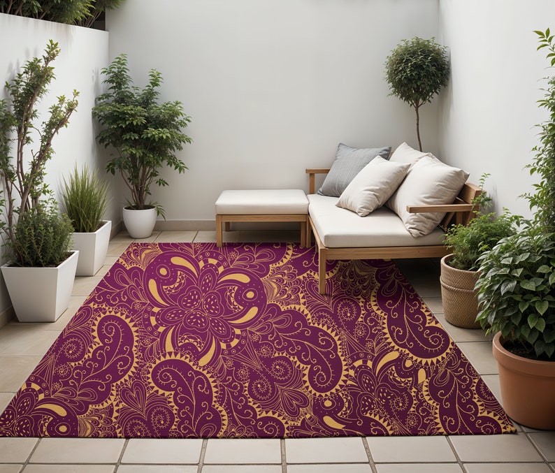 May include: A purple and gold patterned area rug with a floral design. The rug is laid out on a tiled patio with a wooden bench and potted plants.