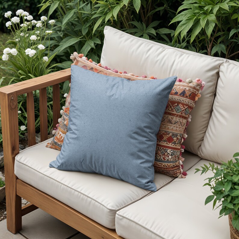 May include: A wooden outdoor sofa with white cushions and three pillows. The pillows are a light blue, a patterned orange and brown, and a pink and orange patterned pillow with tassels.