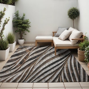 May include: A brown and white patterned outdoor rug with a geometric design. The rug is placed in a patio setting with a white couch and a wooden coffee table.