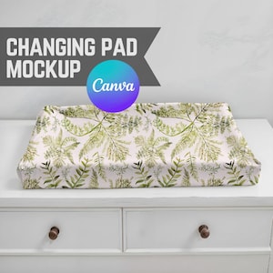 May include: A white changing pad with a green and white floral pattern. The pad is on top of a white dresser with two drawers.