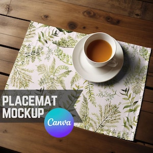 Może przedstawiać: Biały obrus z zielonym wzorem liści i biały spodek z filiżanką herbaty na górze. Obrus leży na drewnianym stole. Tekst "PLACEMAT MOCKUP Canva" znajduje się na obrusie.