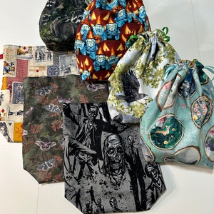 Peut inclure: Un ensemble de sept sacs à cordon avec différents motifs. Les sacs sont en tissu et présentent une variété de motifs, notamment des gnomes, des ratons laveurs, des papillons de nuit, des zombies, des oiseaux et des fleurs.