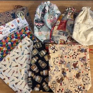 May include: A collection of drawstring bags with various patterns. Designs include guitars, dice, hot air balloons, playing cards, and cartoon characters. The bags are made of fabric and have a drawstring closure.