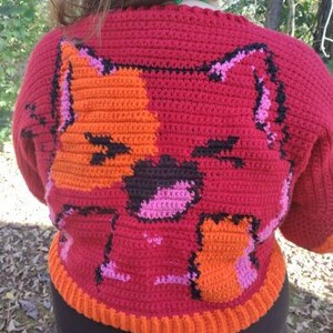 May include: A red crocheted jumper with an orange and pink cat design. The jumper has a ribbed hem and cuffs.