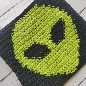 May include: A black and green crocheted pouch with an alien face design. The pouch is made with a textured stitch and has a pink zipper.